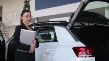 Bir kadın bagajı açık beyaz bir aracın yanında, kişisel lüks arabanın dış ve otomotiv tasarımını sergiliyor. Jest, yüklemeye ya da boşaltmaya hazır olduğunu gösteriyor.
