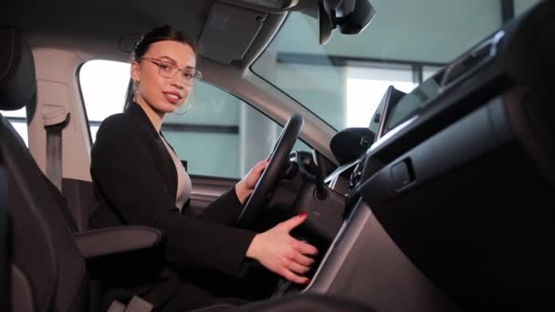女性は車両のドライバーシートに位置し 自動車のデザインと外観の特徴を示しています 彼女は自動車の内側にジェスチャーを作っているのを見ています — ストック動画