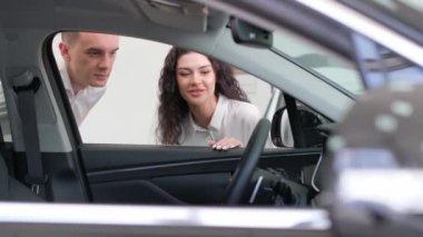 Arabanın içine bakan bir adamla bir kadının yakın çekim videosu. Genç bir çift satın almak için bir araba seçer. Yeni bir araba alıyorum.
