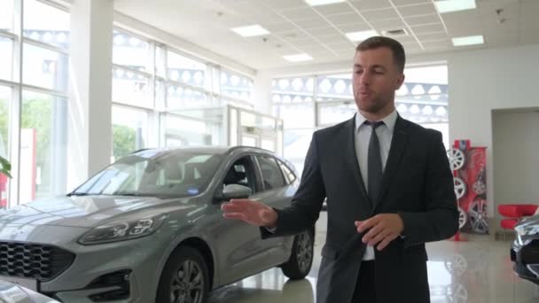 ビジネスススーツの若いセールスマンコンサルタントは 車のショールームを歩いている間に新しい車を提示します 高価な現代車の車のショールーム — ストック動画