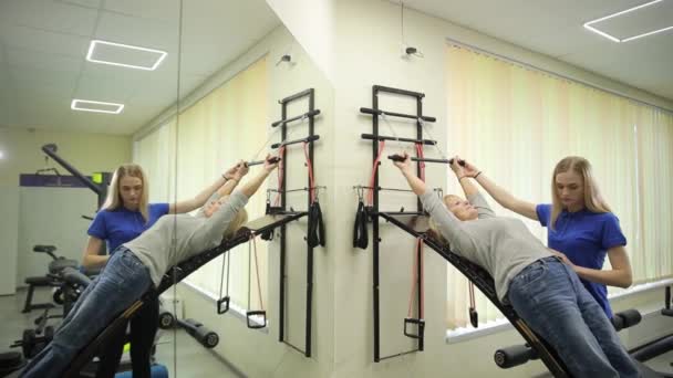一个女人正在通过在健身房的锻炼来帮助一个男人锻炼身体 他们把注意力集中在大腿和膝关节的力量 平衡和为休闲和娱乐进行的巡回训练上 — 图库视频影像