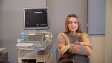 Muayenehanede ultrason cihazının yanında oturan genç bir kızın portresi. Muayene edilen bir kız. Doktor randevusunda hamile bir kız.