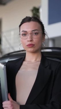 Bir kadın bagajı açık bir aracın yanında, otomotiv tasarımını ve arabanın lastik, ayna ve kapısı gibi dış özelliklerini sergiliyor. Dikey video