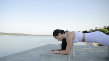 İki kadın, göl kenarındaki büyük taşlar üzerinde kalas egzersizi yapıyor. Bir yaz gününde açık hava fitness
