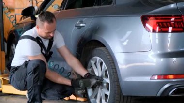Bir kişi garajdaki bir aracın tekerleğini değiştiriyor, arabanın rutin bakımının bir parçası. Bu, araba kullanırken güvenli ve optimal performansı sağlamakta yardımcı olur