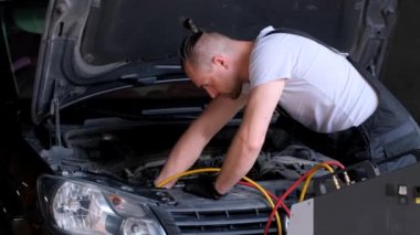 Bir adam otomotiv garajında kaputun altındaki bir aracı tamir ediyor. Otomotiv aydınlatma, ızgara, tampon ve lastik tasarımı üzerinde çalışıyor.