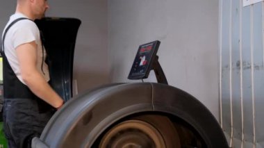 Bir adam garajdaki bir makinenin lastiğini dengelemek için otomotiv ekipmanı kullanıyor.