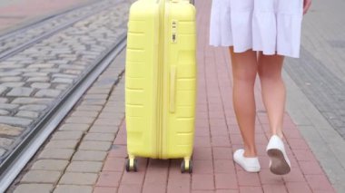 Genç bir kadının incecik bacakları kaldırım taşlarında yürüyor, sarı bir bavul çekiyor. Turist kadın seyahat ediyor. Bagaj. Sarı bavul.