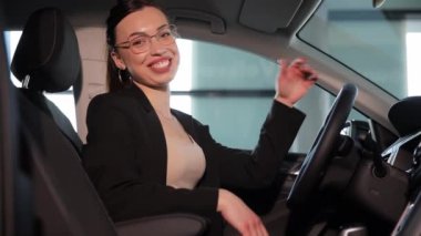 Çok mutlu gülümseyen bir iş kadını pahalı bir arabanın içinde oturuyor. Takım elbiseli bir kadın arabada oturur ve kameraya gülümser..