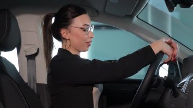 Kendine güvenen genç iş kadını arabanın içinde oturup test sürüşü yapıyor. Yeni bir arabanın gözden geçirilmesi. İş stili ve takım elbiseli bir kadın arabada oturuyor.