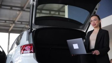 Arabanın bagajında tabletle oturan seksi genç bir iş kadını. İş kadını bir arabanın bagajında otururken internette çalışıyor..