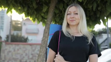 Bir yaz günü bir ağacın altında arka planda jimnastik minderiyle duran orta yaşlı, sportif bir kadın. Spor aletleri olan sıska bir kadın..