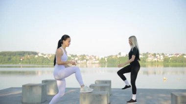 Gölün arka planında iki kadının spor eğitimi. Sıcak bir yaz gününde aktif fitness egzersizleri. Sağlık, hareket kavramı.