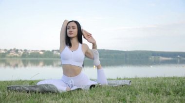 İnce, güzel bir esmer, yoga dersleri sırasında sabah gölünün arka planına doğru esneme hareketleri yapar. Göl kenarında açık hava yogası.