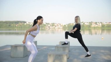Gölün arka planında iki kadın için aktif fitness eğitimi. Aktif fitness egzersizleri. İki kadın şınav çekiyor. Sağlık, hareket kavramı.