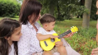 Bir anne küçük oğluna parkta küçük bir gitar çalmayı öğretir. Yüksek kalite 4k görüntü