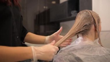 Kadın müşteri, bir kuaför renkçisinin sandalyesinde oturuyor ve saçını bir güzellik salonuna boyuyor, yakın plan bir portre. Yüksek kalite 4k görüntü