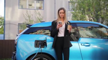 Bir kadın elektrik yüklü bir arabanın yanında duruyor, çevre dostu doğasını ve şarj sürecini elektrikle vurguluyor.