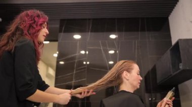 Güzellik salonunda, bir kuaför saçlarını yıkadıktan sonra saçlarını ıslatan sarışın müşterileri tarıyor. Yüksek kalite 4k görüntü