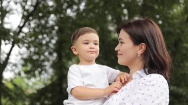 Oğlunu kucağında tutan genç bir anne, yaz parkında birlikte yürüyorlar. Yüksek kalite 4k görüntü