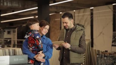 Çocuklu genç bir aile, inşaat süpermarketinde dururken seramik fayansları dikkatlice seçiyor. Bir aile, yeni bir evin banyo ve zeminini yenilemek için fayans seçer.