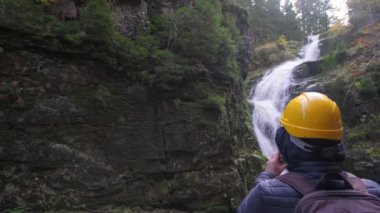 Sarı şapkalı bir adam görkemli bir şelaleyi keşfeder, güzelliğinden büyülenir. Anı korumak için fotoğraf çekiyor.