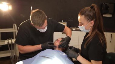 Bir erkek ve bir kadın dişçi muayenehanesinde bir kadının yüzüne bakıyorlar. Yüksek kalite