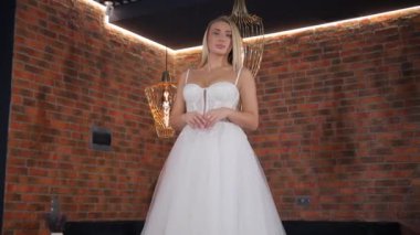 Göz kamaştırıcı beyaz gelinlikli gelin tuğla bir duvarın önünde gülümsüyor, mutluluk saçıyor. Flaşlı fotoğraf onun neşeli hareketini yakalıyor.