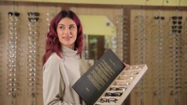 Bir kadın, ahşaptan yapılmış bir göz teçhizatı sergisinin önünde, müzik aletine benzeyen bir deseni olan bir kitap tutuyor. Oda sanat ve müzik temalı dekorlarla dolu.