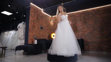 Bir gelin heyacanlı bir şekilde düğün salonunda çeşitli gelinlikleri dener, flaşlı fotoğrafçılık onun büyük günü için mükemmel elbiseyi seçerken mutluluğunu yansıtır.