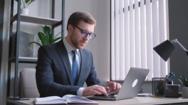 Takım elbiseli bir profesyonel, görevini yaparken motivasyon ve kararlılığı somutlaştıran bir dizüstü bilgisayarla çalışma masasında özenle çalışır.