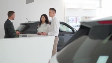 Bir çift galeride lüks bir araba hakkında bir araba satıcısıyla konuşuyor. Kaput, araç kapısı, dış tasarım, ayna ve aydınlatma gibi otomotiv özelliklerine bakıyorlar.