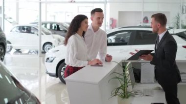 Bir erkek ve bir kadın, otomotiv tasarımları ve sergilenen tekerleklerle çevrili bir araba galerisinde araç seçeneklerini tartışıyorlar.