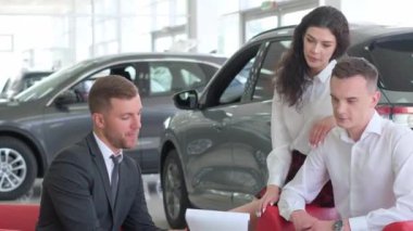 Bir adam ve bir kadın araba galerisinde dizüstü bilgisayarı inceliyor, otomotiv tasarımına hayran kalıyor ve aracın özelliklerini tartışıyorlar.