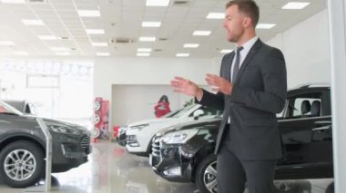 Takım elbiseli ve kravatlı bir adam araba galerisinde müşteriyle otomotiv tasarımını tartışıyor.