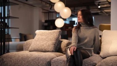 Gri kazaklı güzel bir kadın mobilya mağazasında bir kanepede oturuyor. Yüksek kalite 4k görüntü