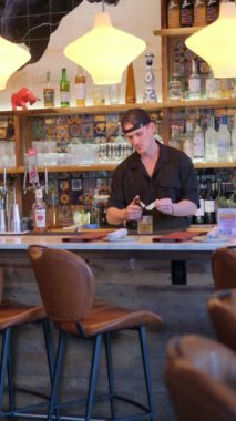 Canlı bir restoranda, bir barmen canlandırıcı bir içecek hazırlar. Karışımın sanatını ve canlı sosyal etkileşimlerini yakalar.