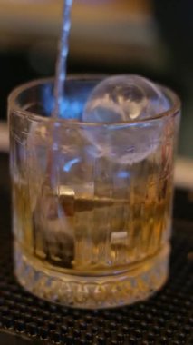 Bu videoda bir bara dökülen viski sanatı sergileniyor. Buzlu bardakların yakın çekimleri ve aralıksız akan zengin kehribar viskisi.