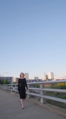 Zarif siyah elbiseli bir kadın pitoresk bir köprüde yürüyor, nefes kesen şehir manzarasına hayran olmak için duruyor, yalnızlığı ve sofistikeliği anımsatıyor.