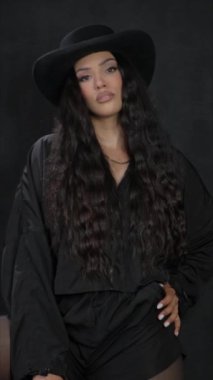 Siyah elbiseli, kovboy şapkalı ve ceketli kendine güvenen bir kadın şık bir klipte cesur kişiliğini sergiliyor.