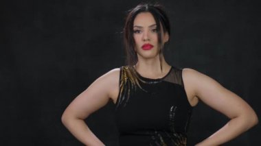 Videoda siyah ve altın rengi bir elbise giymiş kendinden emin bir kadın, güç ve zarafet saçarak izleyicileri güçlendirme hikayesine davet ediyor.