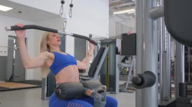 Bir kadın spor salonunda spor aleti kullanarak antrenman yapıyor. Forma girme ve kişisel refahı konusundaki kararlılığını ve kararlılığını gösteriyor.