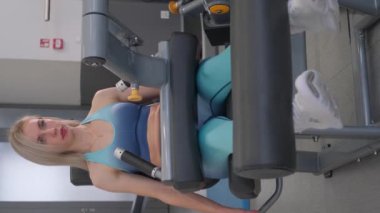 Bir kadın spor makinelerinde bacak egzersizleri yapıyor, güç eğitimini vurguluyor. Enerjik bir spor salonundaki bacak uzatma makinesinde uygun formu gösteriyor.