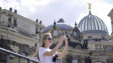 Bir kadın akıllı telefonuyla şehrin güzelliğini yakalar, çarpıcı bir binayı ve muhteşem bir kubbenin detaylarını fotoğraflar.
