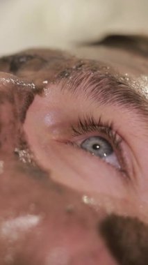 Bir adam kaplıcada yüz bakımı görüyor, kirpiklerine, çenesine, sakalına ve kulaklarına odaklanıyor.. 