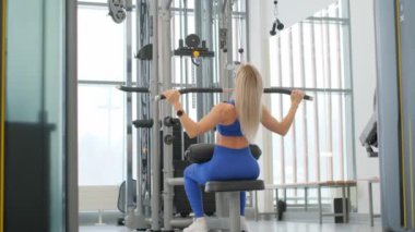 Bir kadın spor salonundaki bir spor makinesine rahatça oturmuş fiziksel kondisyonunu ve refahını arttırmak için egzersiz yapıyor.