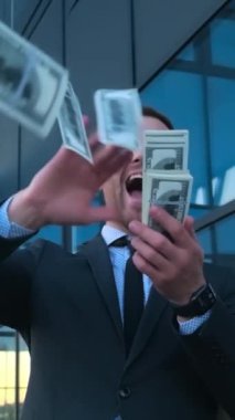 Çılgınca mutlu genç iş adamı dolarları saçıyor. Yüksek kazanç. Yüksek maaş. Dikey video. Mutluluğun olumlu duyguları