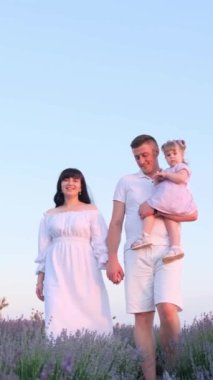 Lavanta tarlasında bebeği olan mutlu, genç bir aile. Gökyüzüne karşı lavanta tarlasında aile fotoğrafı çektirmek. Dikey video