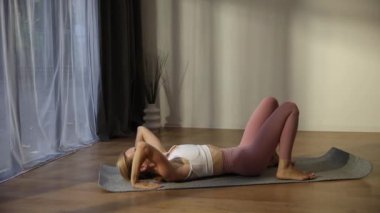 Huzurlu bir videoda, rahat oturma odasında yoga yapan bir kadın poz vererek, sükunet ve farkındalığı somutlaştırıyor.