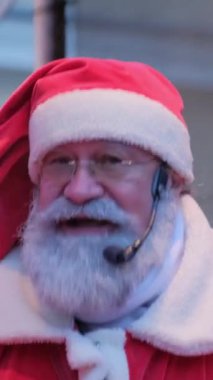 Telefon için video. Yaşlı, kır saçlı bir Noel Baba arkada dururken mikrofona duygusal bir konuşma yapıyor. Noel Baba insanlara seslenir ve onlara mutlu Noeller diler.